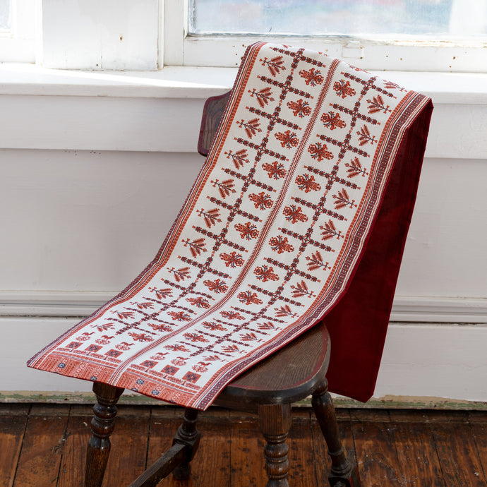 Decorative red and black Palestinian tatreez patterned table runner on a wooden table.