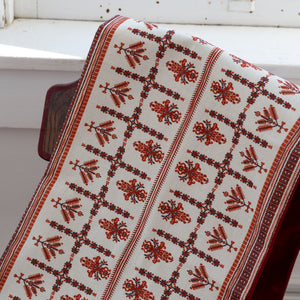 Decorative red and white Palestinian tatreez patterned table runner draped over a chair by a window.