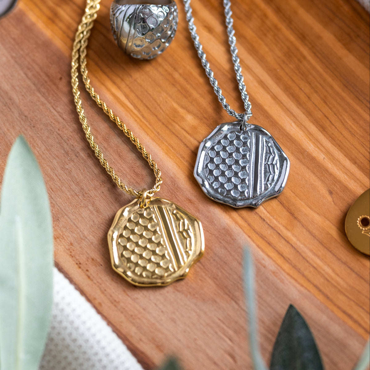Gold and silver necklaces with intricate Palestinian kuffiyeh/keffiyeh pendants on a wooden surface.