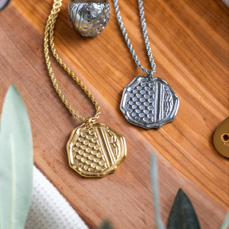 Gold and silver necklaces with intricate Palestinian kuffiyeh/keffiyeh pendants on a wooden surface.
